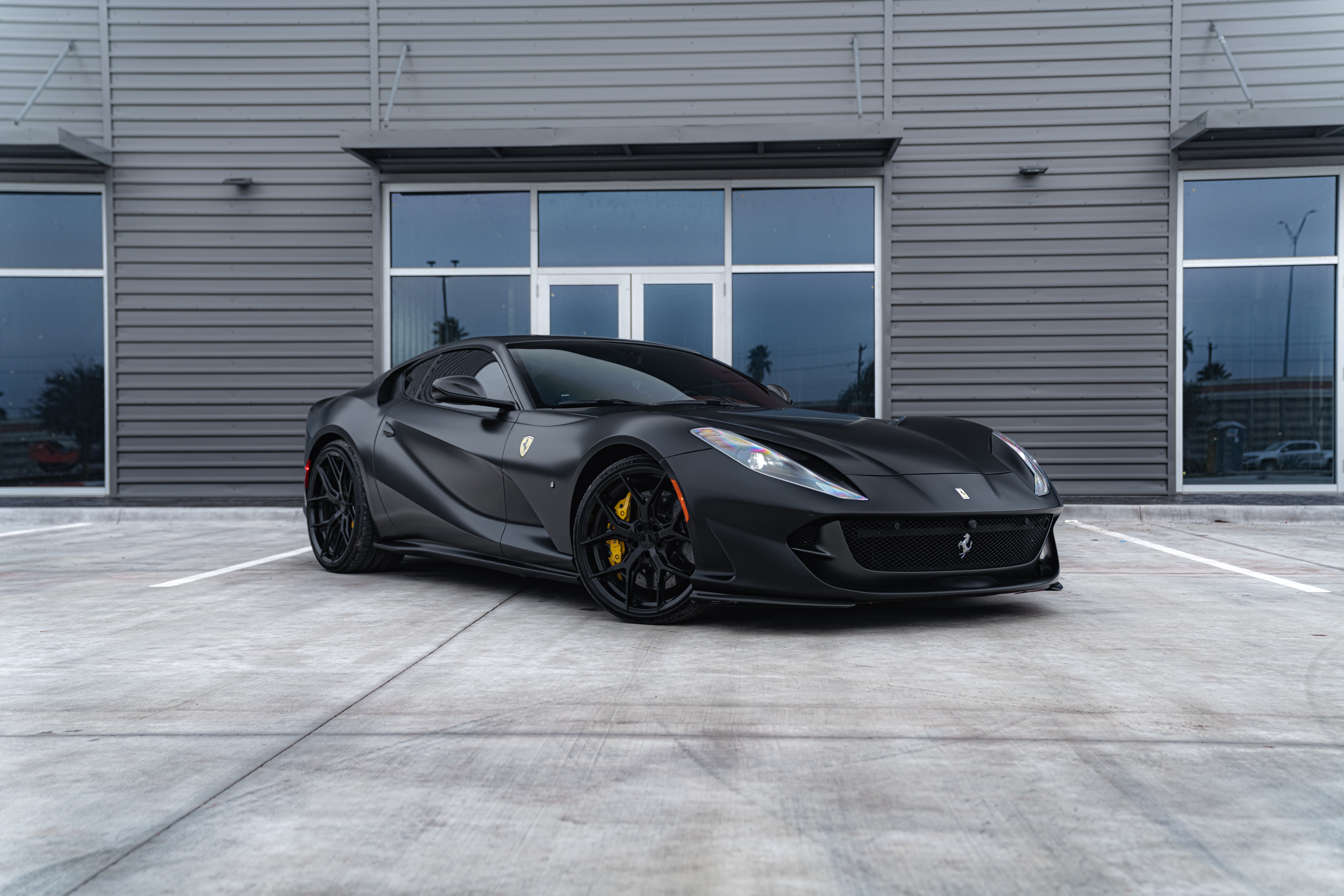 Black Ferrari parked outside a modern garage.