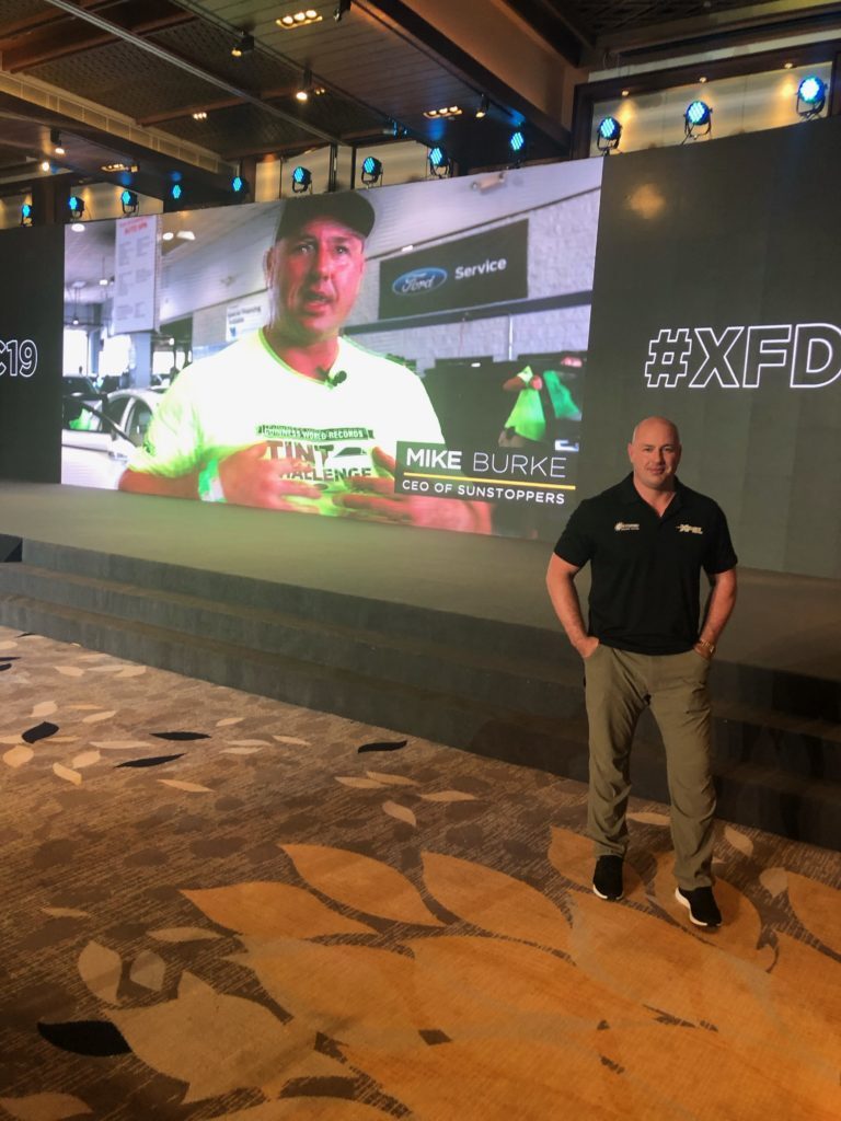 Mike Burke poses in front of a video screen during XPEL's flagship Asian Dealer Conference in April of 2019.